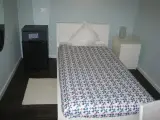 Mininevera negra junto a la cama individual y alfombra blanca sobre el suelo de madera